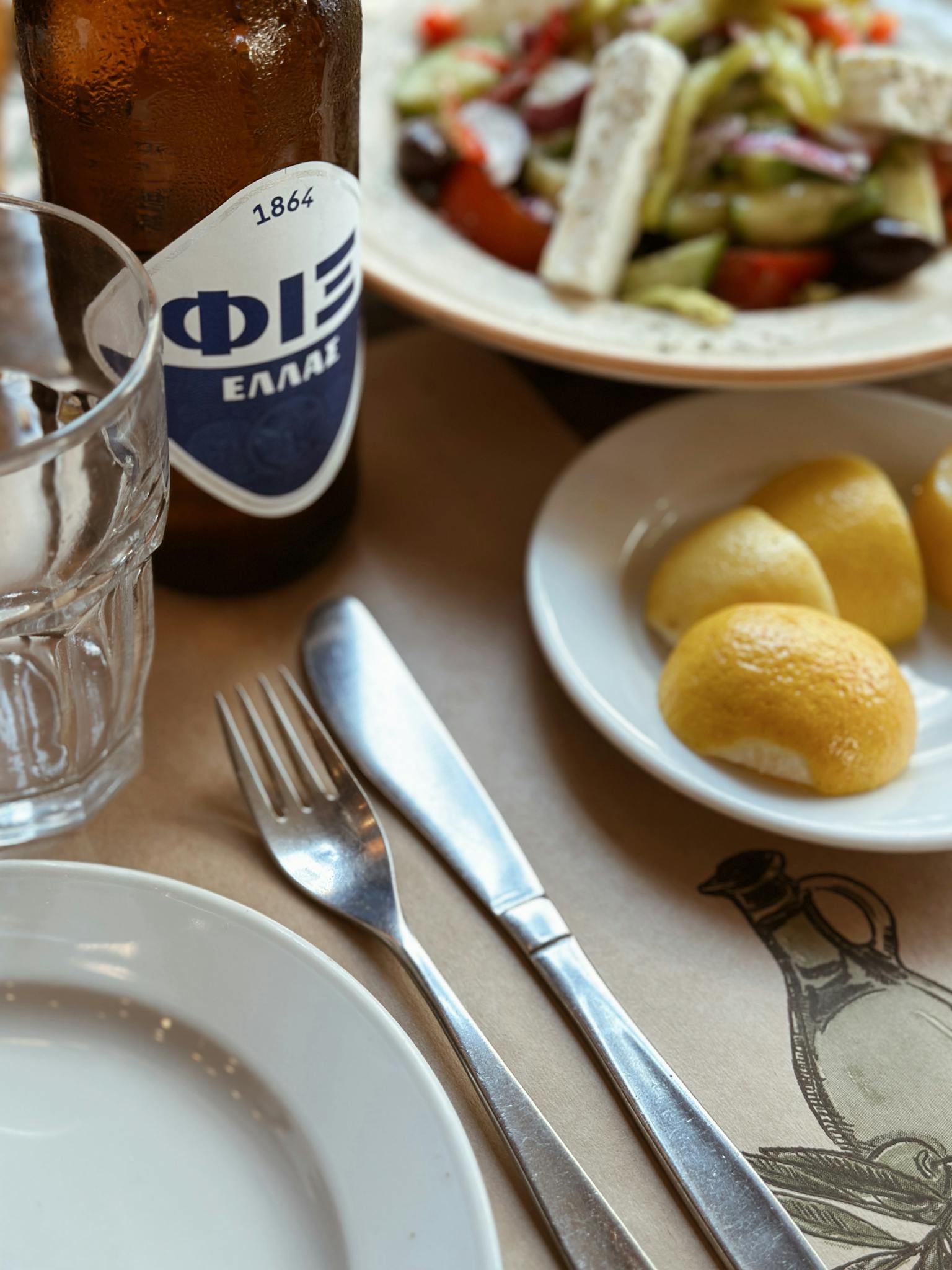 A Greek dining table setting with lemon slices, salad, and a beer bottle.