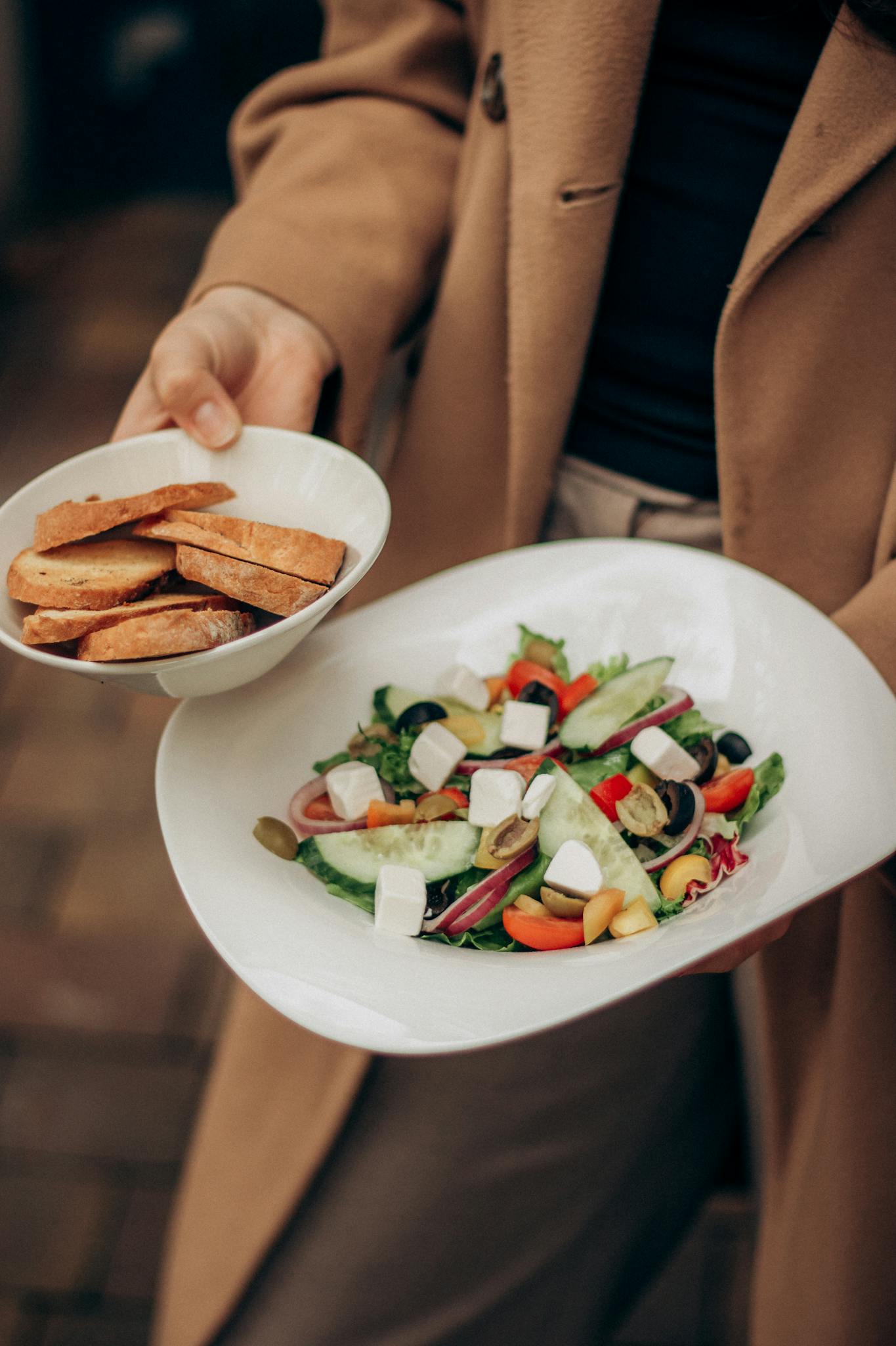 A vibrant Greek salad featuring fresh vegetables, feta cheese, and crisp bread slices, served outdoors.