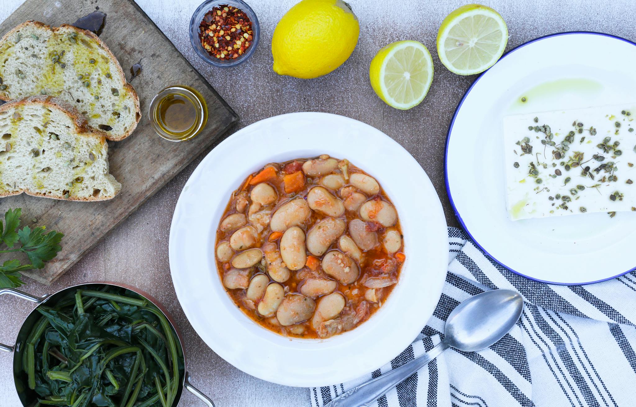 Top view of a Greek meal featuring white beans, bread, feta, and spices.